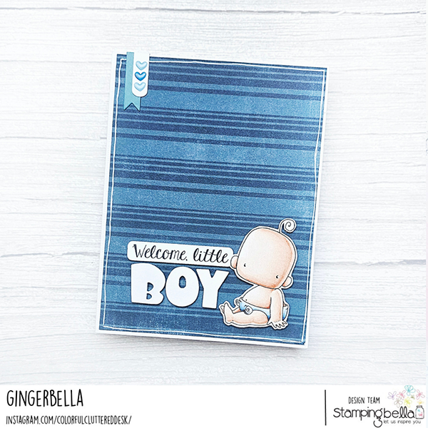 "Handmade baby card by Gingerbella featuring Stamping Bella Baby Boy & Girl and Baby Sentiment Set cling mounted rubber stamp sets. The card has a blue striped background with a small blue ribbon tab at the top left corner adorned with three heart icons. The main feature is a cute illustration of a baby boy sitting in a diaper with a safety pin, positioned at the bottom right. The text on the card reads 'Welcome, little BOY' with 'BOY' in large, bold white letters.