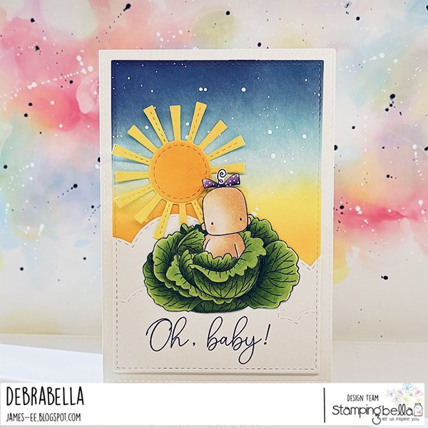 This handmade card design features the Stamping Bella Cabbage Patch Boy & Girl and Baby Sentiment Set cling mounted rubber stamp sets. The card showcases a cute baby with a small purple bow on their head, sitting inside a green cabbage. The background has a gradient sky transitioning from dark blue at the top to yellow and orange near the horizon, with a bright yellow sun and rays. The bottom of the card has the text 'Oh, baby!' written in elegant script. The card is set against a colorful, abstract background with splashes of pink, blue, and yellow. Card design is by Debrabella from the Stamping Bella design team.