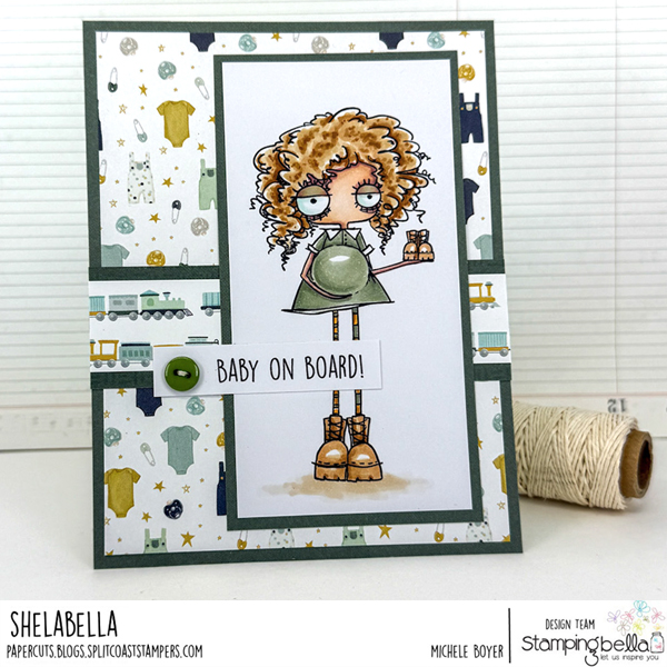 Handmade card design featuring Stamping Bella Oddball Baby on the Way cling mounted rubber stamp and Baby Sentiment Set cling mounted rubber stamp set. The card showcases a whimsical illustration of a character with curly hair, large eyes, and a green dress, holding a pair of baby boots. The character has a round belly, indicating pregnancy. The card is decorated with patterned paper featuring baby-themed icons such as onesies, stars, and toy trains. A sentiment strip with the text 'BABY ON BOARD!' is attached to the card with a green button embellishment. Card designed by Michele Boyer as part of the Stamping Bella design team.