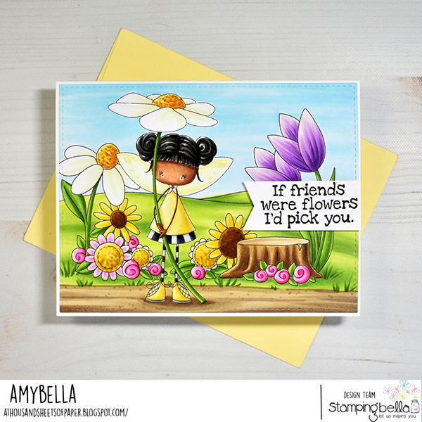 Handmade greeting card featuring Stamping Bella Whimsabella DaisyDream, Hello Spring Sentiment Set, and Spring Backdrop cling mounted rubber stamps. The whimsical design shows a fairy girl holding a large daisy, surrounded by colorful flowers, tree stump, and a sentiment 'If friends were flowers, I'd pick you.' Bright blue sky and green landscape create a cheerful scene. Displayed on a light yellow envelope. Card design by Amy Young aka Amybella as part of the Stamping Bella design team.