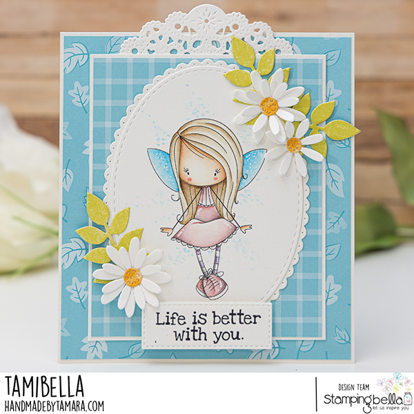 Handmade greeting card featuring a whimsical fairy girl with blue wings, created using Stamping Bella Whimsabella FlitterFly and Spec-Tacular Together Sentiment Set cling mounted rubber stamps. The card has a blue and white color scheme with a checkered background, adorned with white daisies and green leaves. The sentiment 'Life is better with you.' is prominently displayed at the bottom. The card is embellished with a delicate white doily at the top. The design is by Tamibella, part of the Stamping Bella design team.