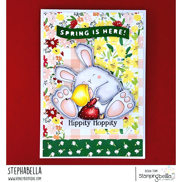 Handmade greeting card featuring a cute bunny and girl hugging, created using Stamping Bella Bundle Girl loves Bunny Wobbles cling mounted rubber stamp. The card has a floral background with yellow, red, and green patterns, and includes the text 'SPRING IS HERE!' at the top and 'Hippity Hoppity' at the bottom. Card designed by Stephabella from the Stamping Bella design team."